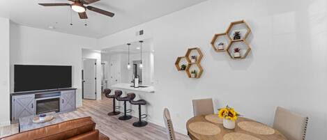 A modern living room with a flat-screen TV, leather sofa, and a dining area with a wooden table and chairs.