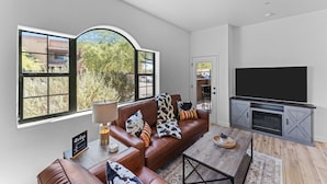 A modern living room with a leather sofa, a flat-screen TV, and large windows offering a view of trees and buildings. - Upscale Southwest Style Condo Tucson (Tucson)