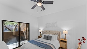 A bedroom with a bed, two bedside tables with lamps, a ceiling fan, a sliding glass door to a balcony, and a decorative wall piece. - Upscale Southwest Style Condo Tucson (Tucson)