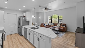 A modern kitchen with white cabinets, a large island, and a dining area with a brown leather sofa. - Upscale Southwest Style Condo Tucson (Tucson)