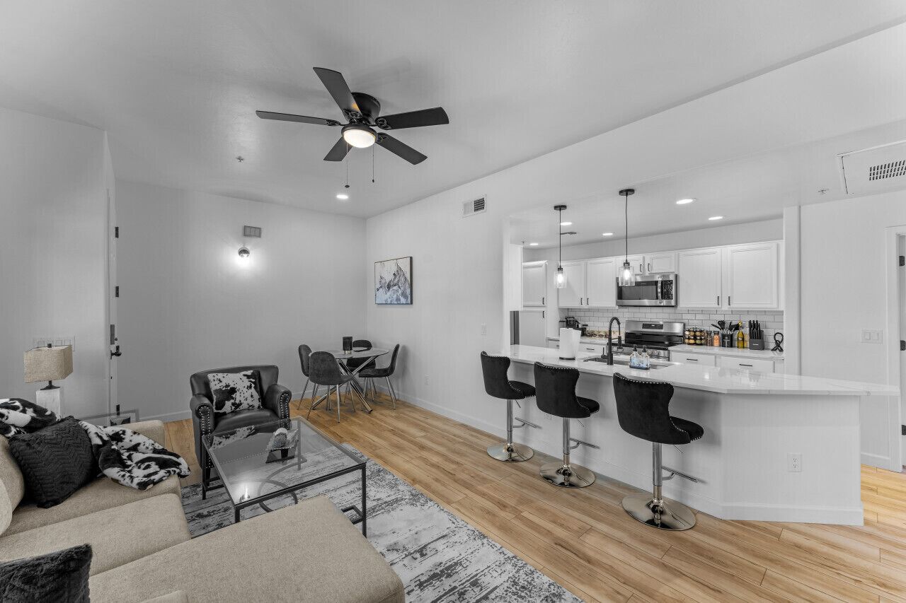 A modern kitchen with white cabinets, a central island with bar stools, and a dining area with a table and chairs.