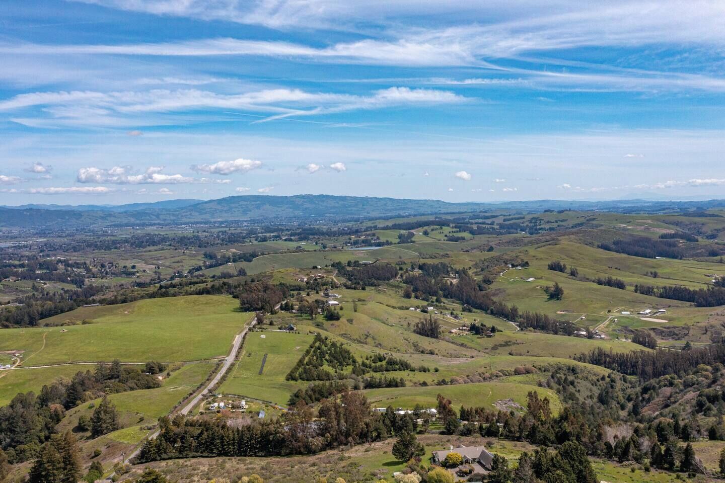 Un paysage rural caractérisé par des collines douces, des maisons dispersées et un ciel dégagé.
