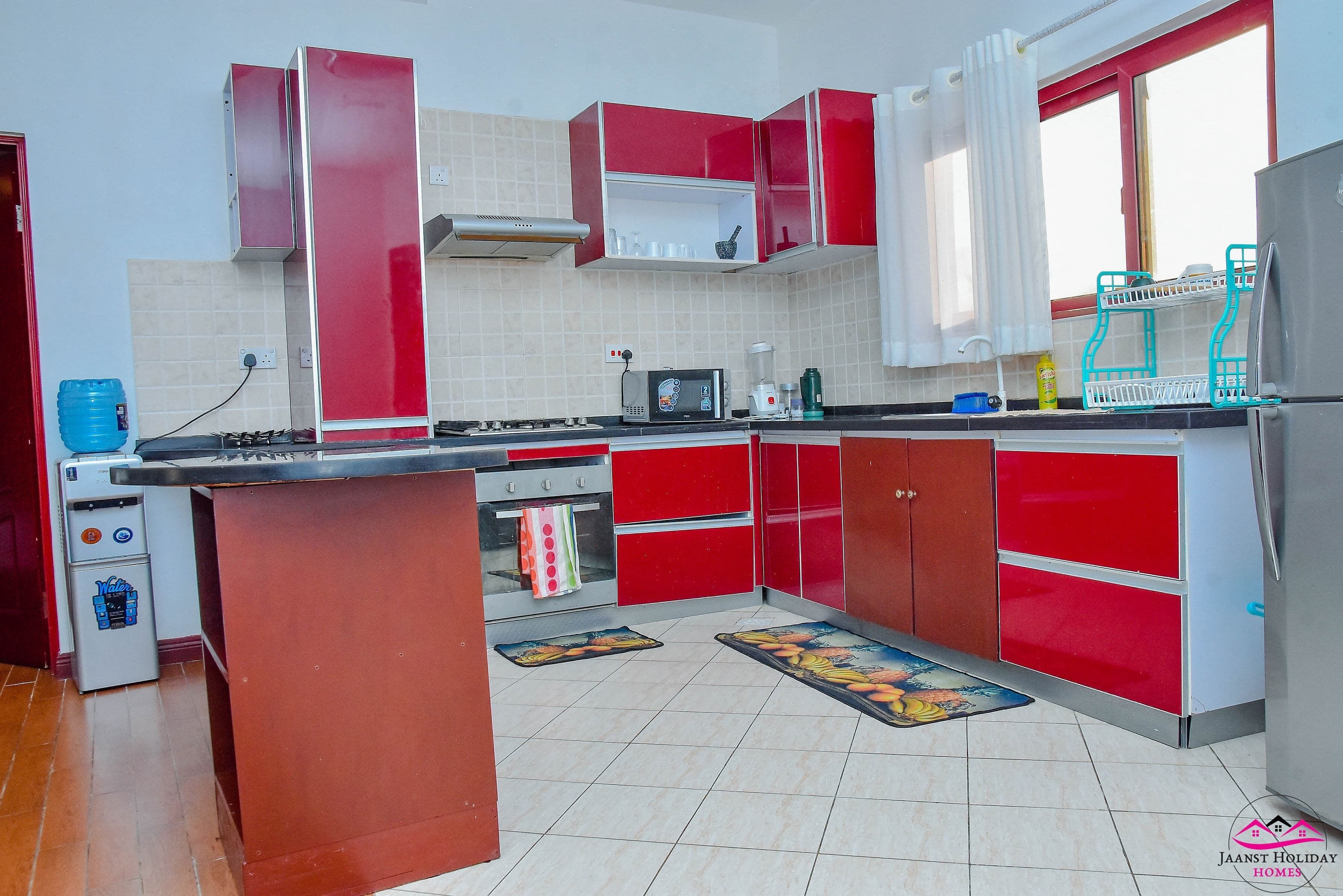 Una cocina con gabinetes rojos, microondas, estufa y dispensador de agua.