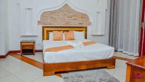 A neatly made bed with a wooden headboard, a small bedside table, and a grey rug on the floor. - Cool Breeze Beachfront Apartments (Mombasa)