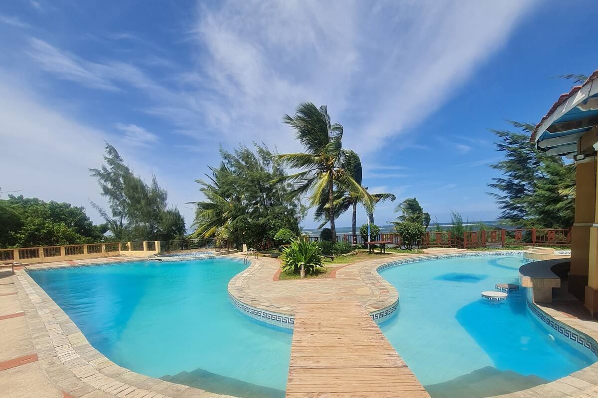 A swimming pool with a wooden deck, surrounded by palm trees and a clear blue sky.