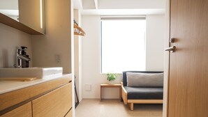 A modern, compact room with a wooden cabinet, a small bedside table with a plant, and a grey sofa. - KABIN Gion (Kyoto)