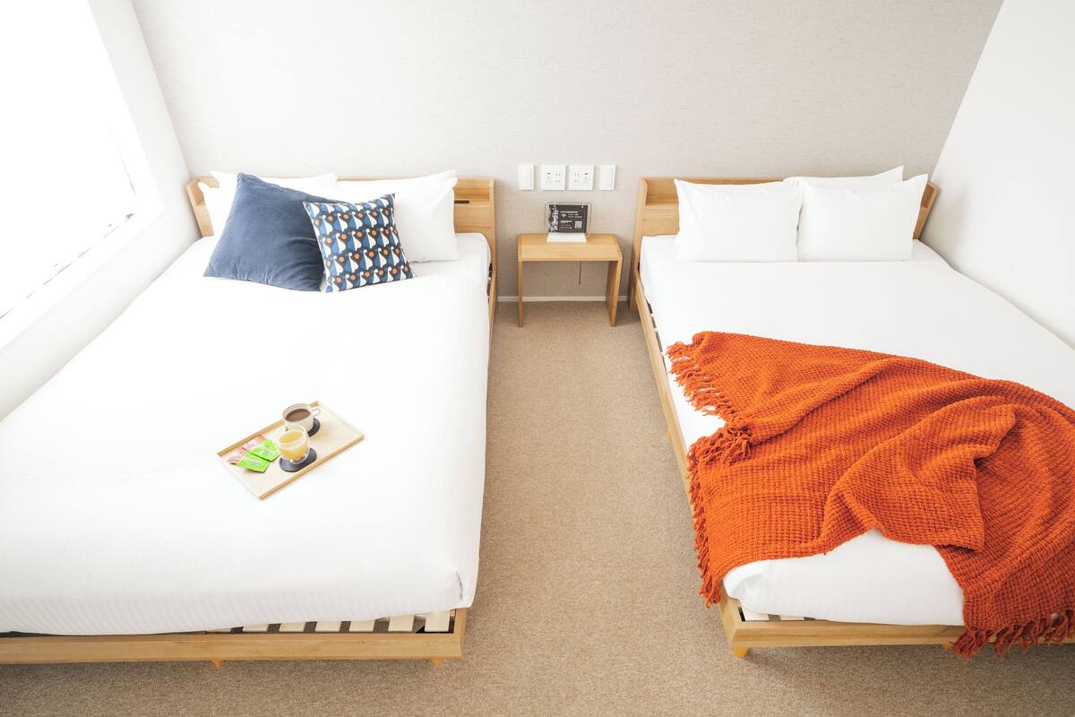 Two single beds with wooden frames, white bedding, and a small bedside table with a book.