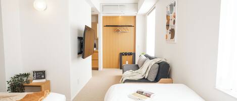 A modern hotel room with two beds, a TV, a wooden wardrobe, a coat rack, and a window with a view.