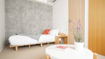 Ein modernes Schlafzimmer mit einem Bett, einem kleinen Tisch mit einem Buch, einer Topfpflanze und einer Holztür.