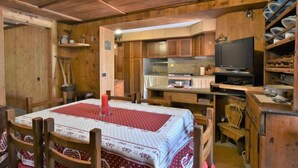 Una habitación acogedora de estilo cabaña, con interior de madera, una mesa de comedor con sillas, un televisor y una zona de cocina.