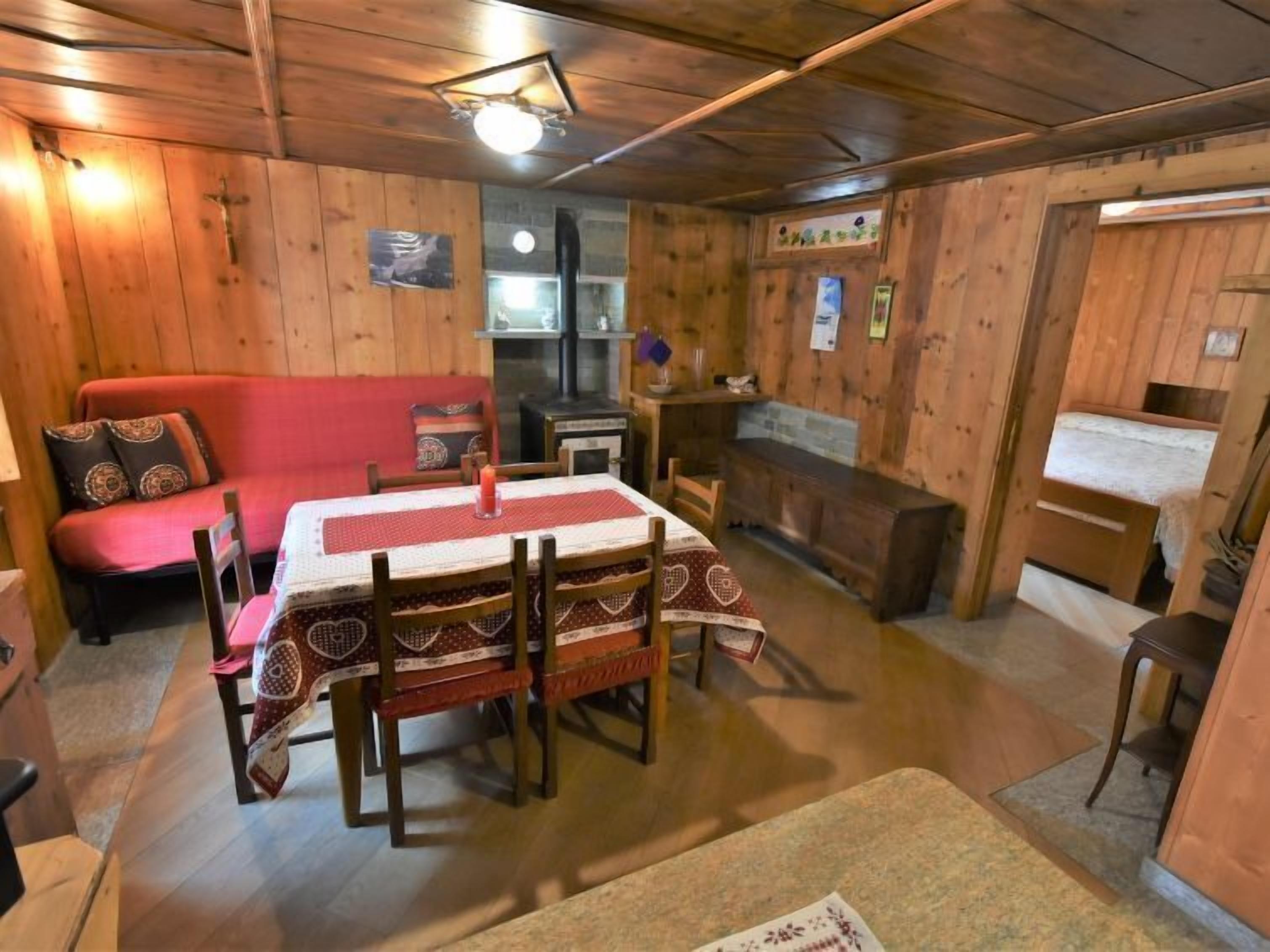A cozy cabin with a wooden interior, a dining table with chairs, a red sofa, a fireplace, and a small kitchen area.