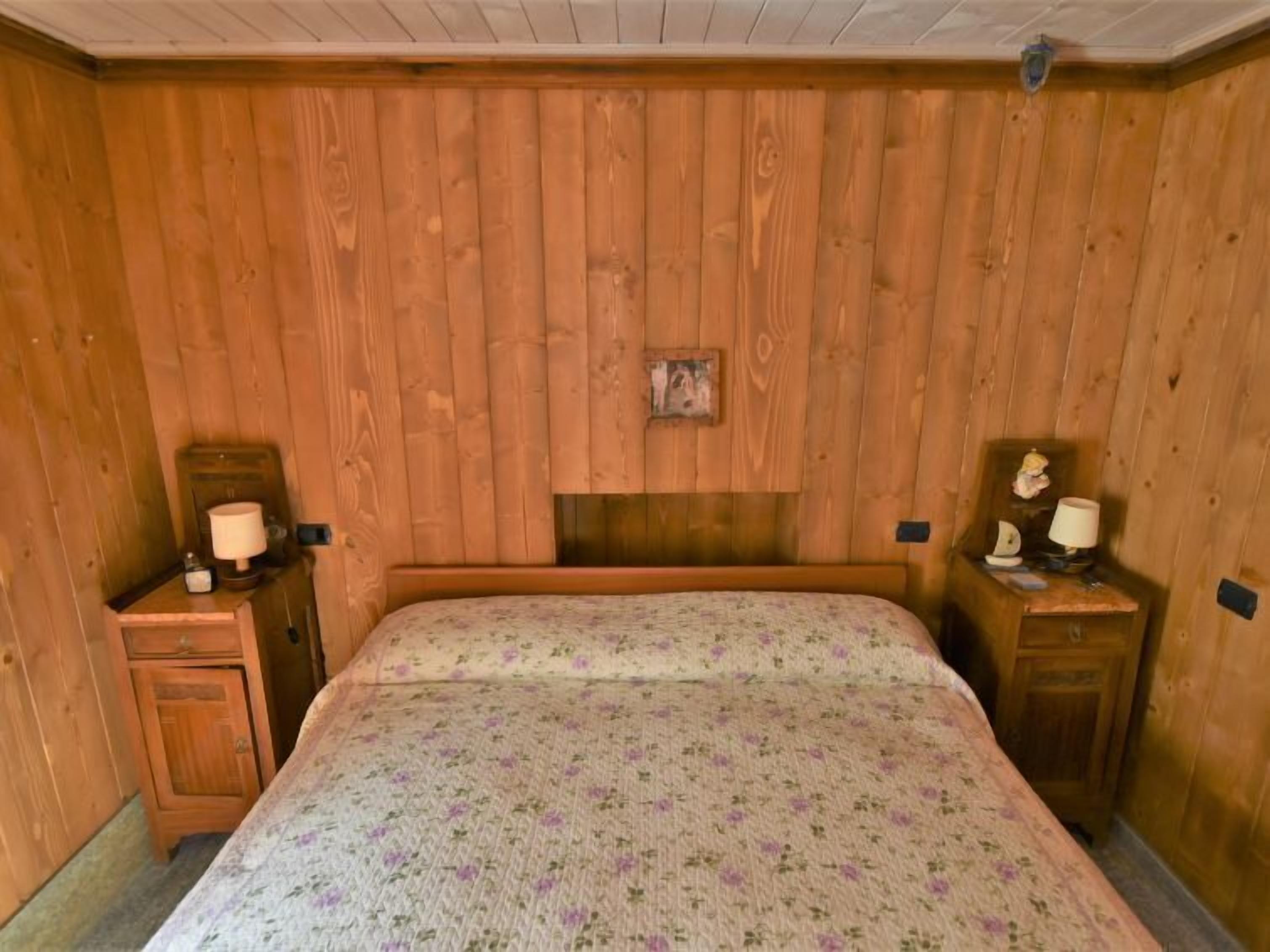 Ein Schlafzimmer mit Holzwänden, einem Bett, zwei Nachttischen und einem kleinen Bild an der Wand.