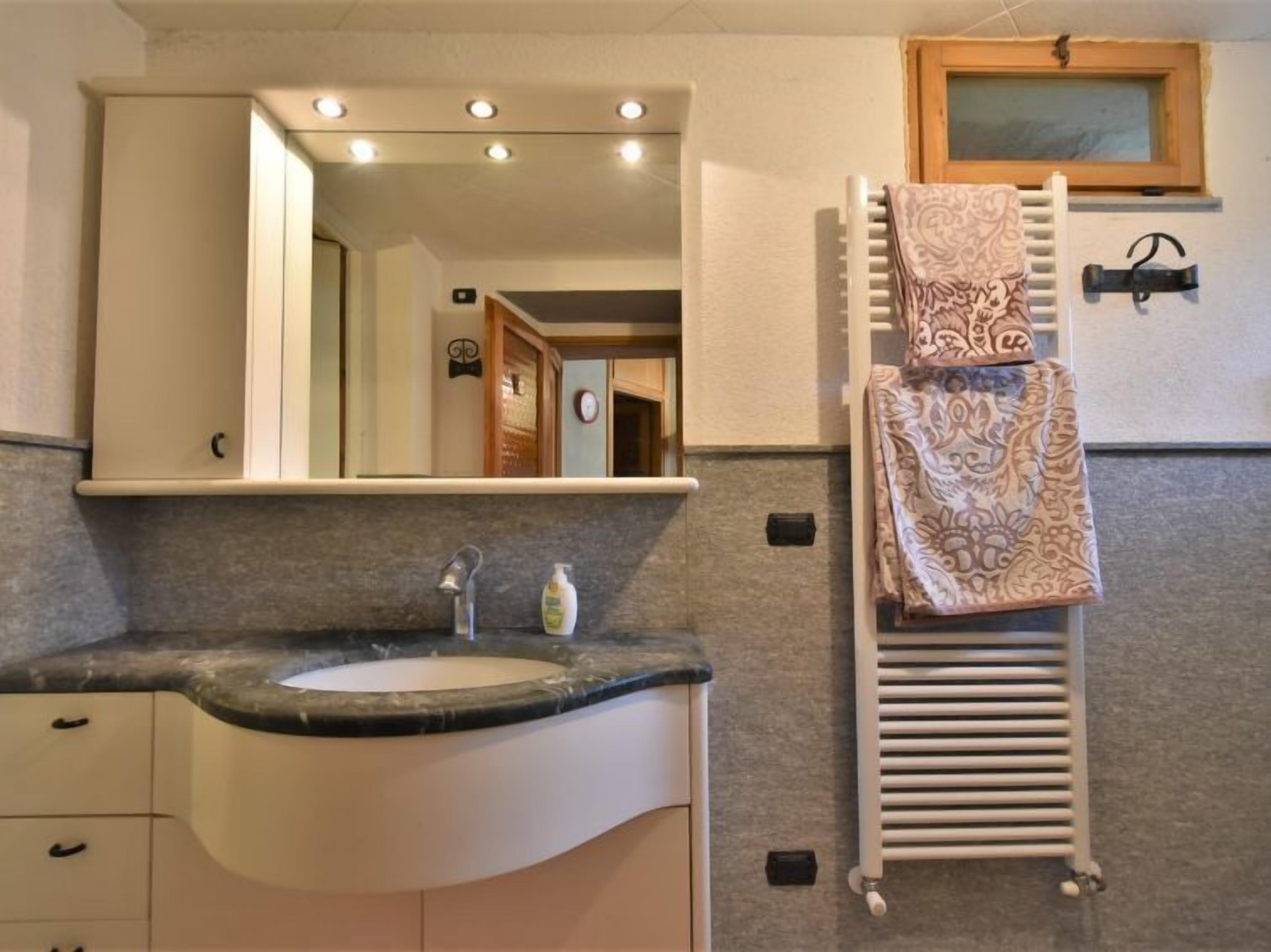 A bathroom with a sink, mirror, towel rack, and a radiator.