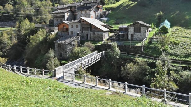 Un edificio de piedra tradicional con techo empinado, rodeado de vegetación exuberante y colinas.