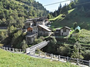 A traditional stone building with a steep roof, surrounded by lush greenery and hills.