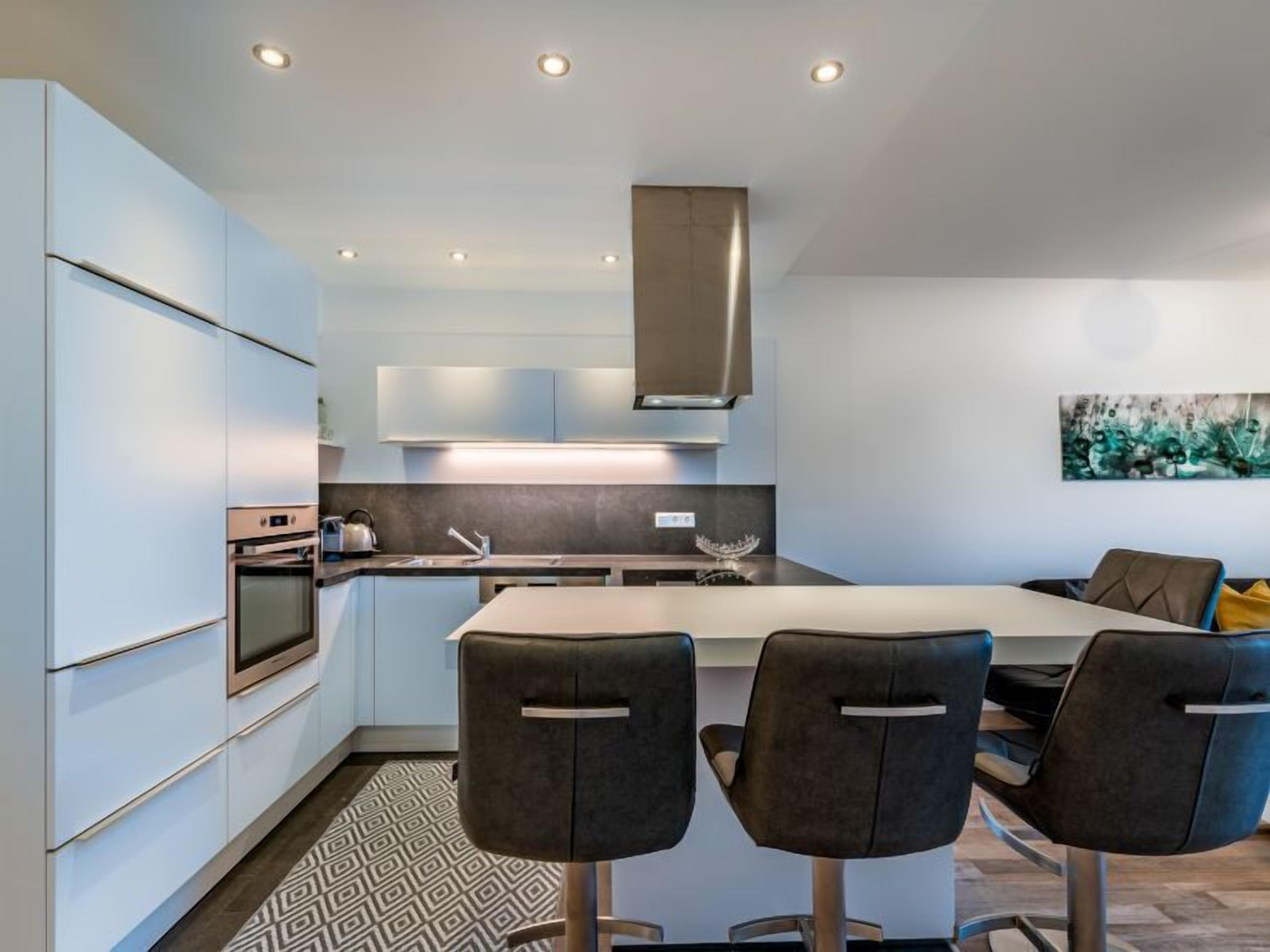 Una cocina moderna con una isla central, electrodomésticos integrados y taburetes de bar contemporáneos.