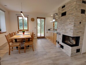 Eine moderne Küche mit Kamin aus Stein, Holzschränken und einem Essbereich mit Tisch und Stühlen.