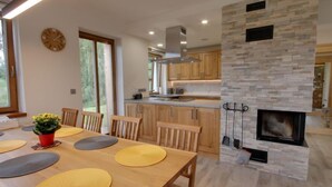 A modern kitchen with wooden cabinets, a stone fireplace, and a dining area with a wooden table and chairs. - U Krále by Interhome (Kořenov)