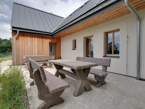 Ein modernes Gebäude mit Holzfassade, einer überdachten Terrasse mit Steinsitzen und großen Fenstern.