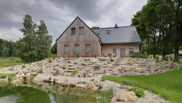 A large wooden house with a sloped roof, situated on a rocky terrain with a pond in the foreground. - U Krále by Interhome (Kořenov)