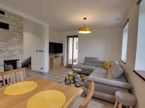 A modern living room with a grey sofa, wooden dining table, and a TV mounted on the wall. - U Krále by Interhome (Kořenov)