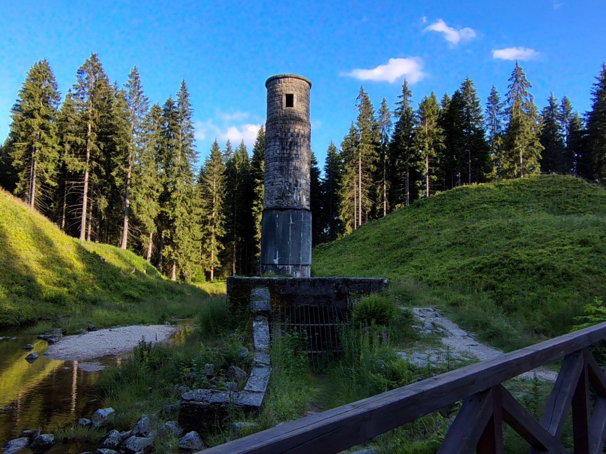 Kivinen torni, jossa on pieni ikkuna, ja sen ympärillä on metsää ja joki.