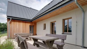 Un bâtiment moderne avec une façade en bois et un patio en béton comprenant une grande table et des bancs.