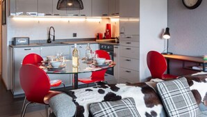 Una cocina moderna con comedor, que incluye una mesa de vidrio, sillas rojas y un sofá estampado con motivos de piel de vaca.
