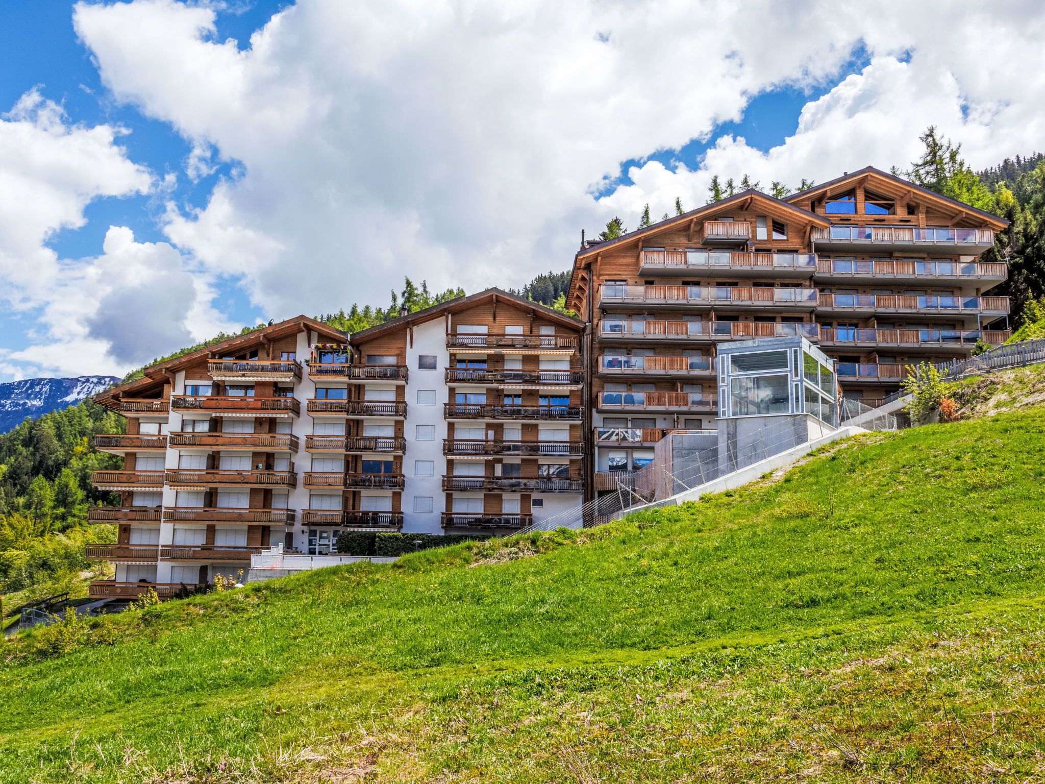 Un hôtel à plusieurs étages, doté de balcons, situé sur une colline et offrant une vue sur les montagnes.