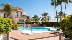 Une piscine entourée de chaises longues, de palmiers et d’un bâtiment dont le toit est recouvert de tuiles.