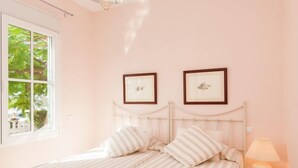 Une chambre à coucher avec un lit, deux tableaux encadrés au mur, une table de chevet avec une lampe et une fenêtre donnant sur des arbres.