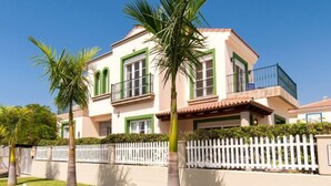 Une maison à deux étages avec une clôture blanche en bois, des encadrements de fenêtres verts et un balcon.