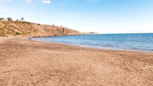 Une plage de sable, un ciel dégagé et une falaise rocheuse en arrière-plan.