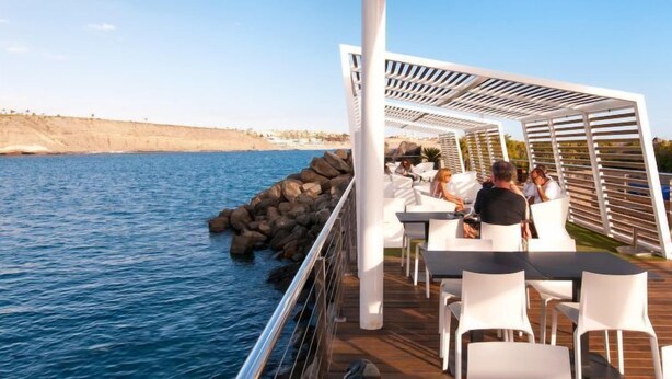 Une terrasse avec des sièges extérieurs donnant sur un plan d’eau, avec une côte rocheuse en arrière-plan.