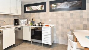 Een moderne keuken met witte kasten, een ingebouwde oven, een kookplaat en twee ramen met uitzicht op groen.