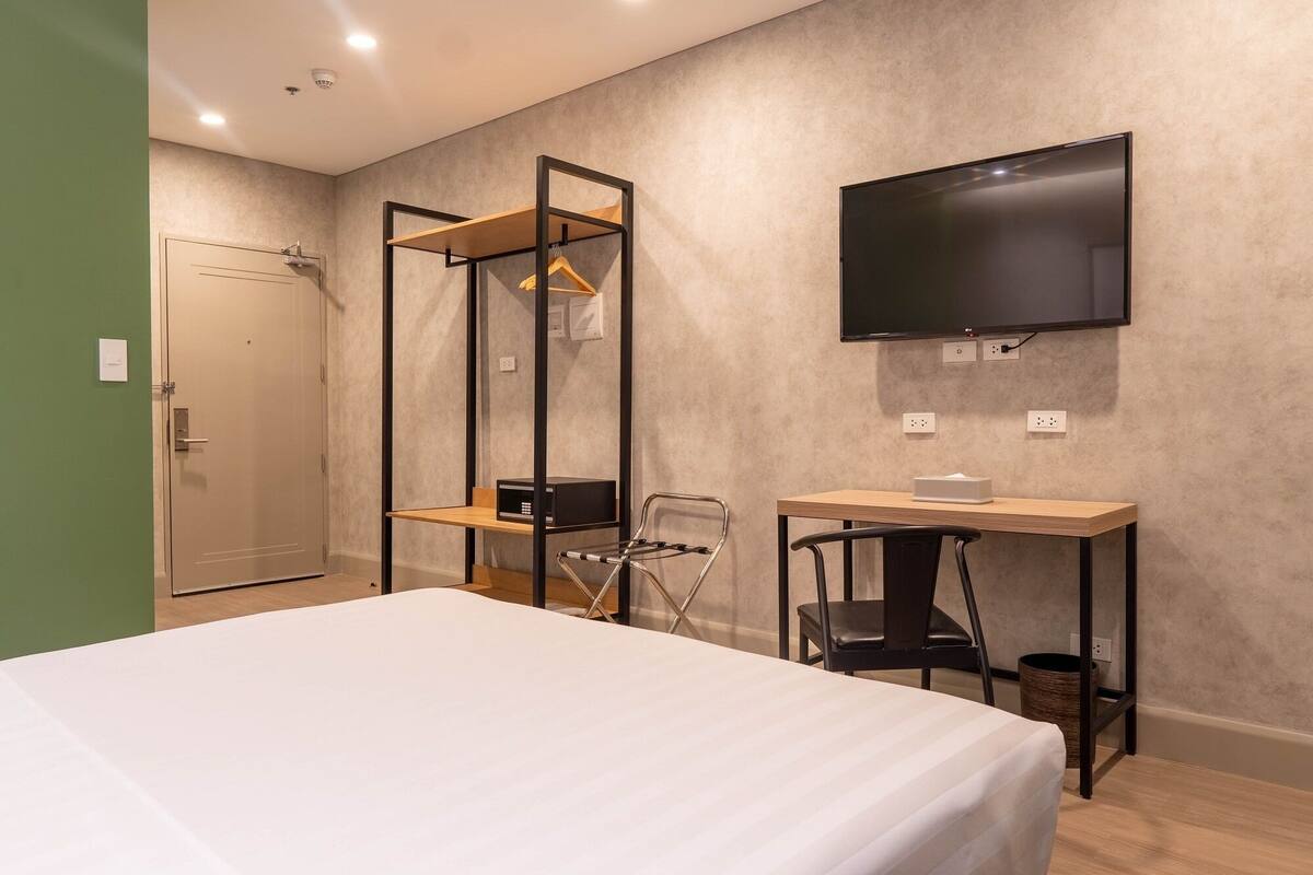 A hotel room with a bed, a desk, a chair, a TV, and a wardrobe.