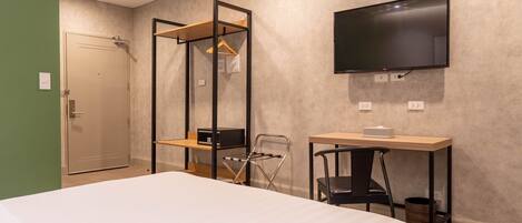 A hotel room with a bed, a desk, a chair, a TV, and a wardrobe.