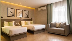 A hotel room with two beds, a sofa, a wall-mounted air conditioner, and framed pictures on the wall. - Primeway Suites Cebu (Cebu City)