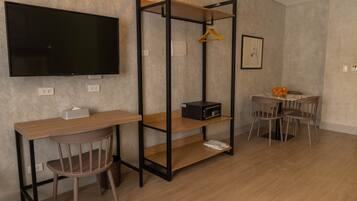 Una habitación moderna con televisor de pantalla plana, un escritorio de madera, una silla, una pequeña mesa con sillas y un mueble con microondas y perchero.