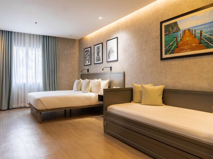 A hotel room with two beds, a large window with curtains, a painting on the wall, and a wooden floor.