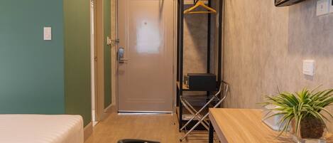 Een kleine hotelkamer met een bed, bureau, stoel, kledingrek en een bloempot.