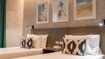 Habitación de hotel con dos camas, una mesita de noche, una lámpara y cuadros en la pared.