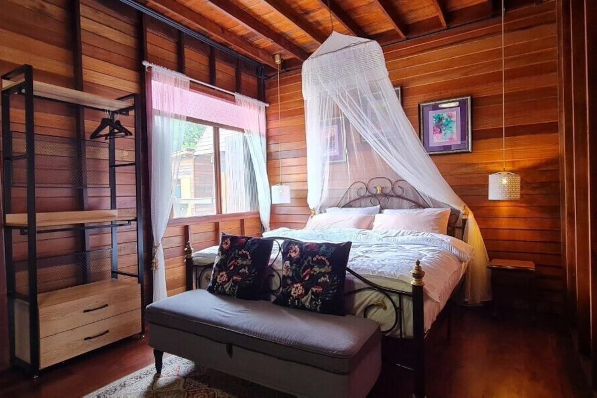 Une chambre dans une cabane en bois, avec un lit, une table de chevet, un banc et une chaise suspendue.
