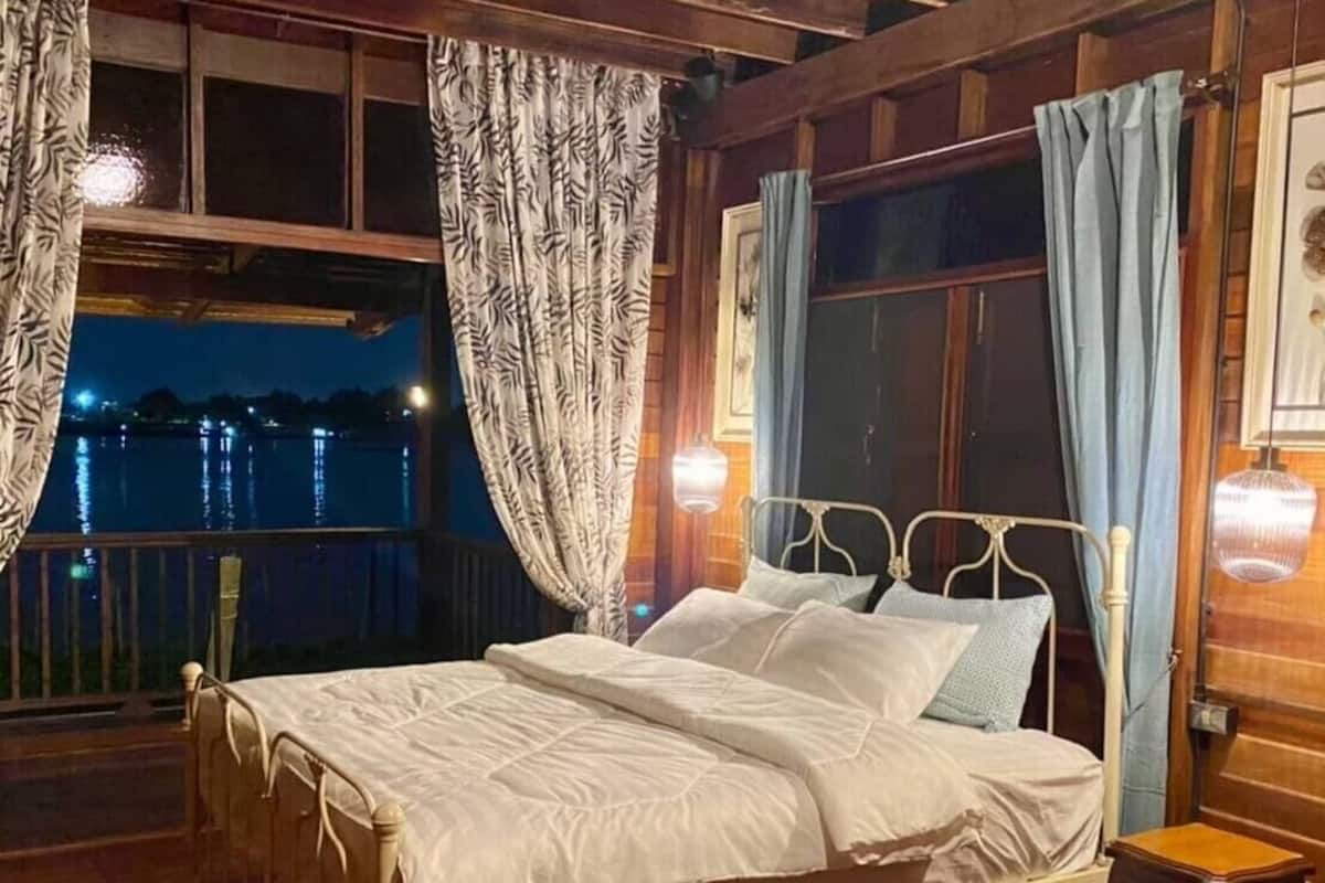 Une chambre à coucher dans une cabane en bois, avec un lit en métal, du linge de lit blanc et une vue sur un lac la nuit.