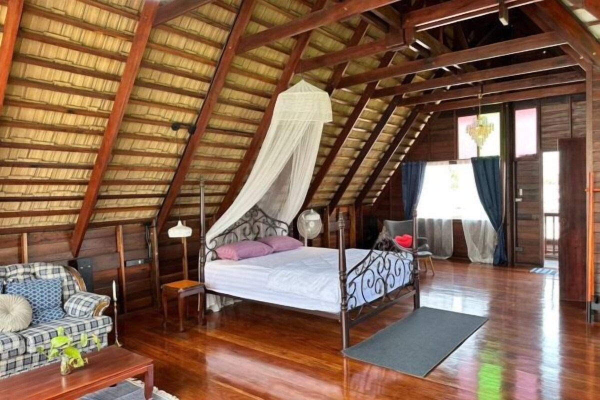 A spacious room with a high ceiling, a bed with a canopy, a sofa, a small table, and a chair.