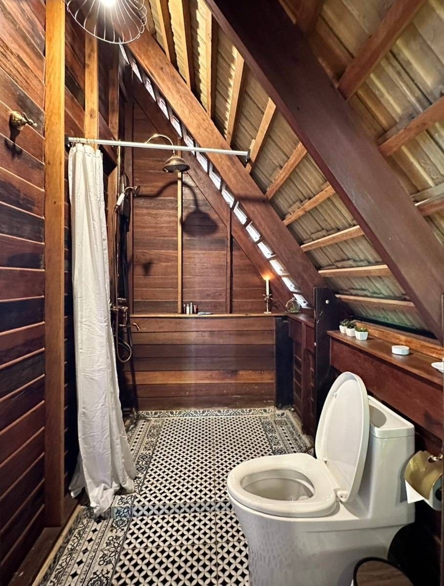 A wooden interior with a sloped ceiling, a toilet, and a shower area.