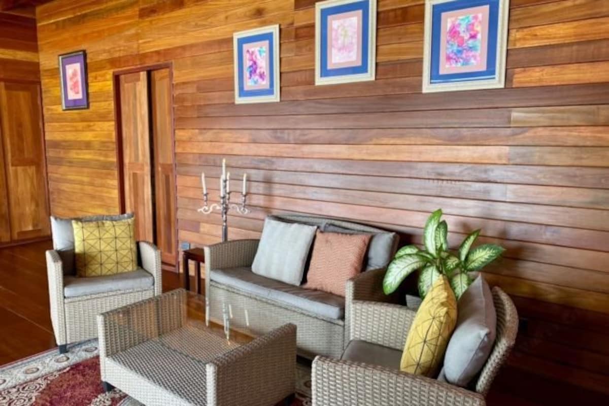 A room with wooden panel walls, a sofa, two armchairs, a coffee table, and a decorative plant.