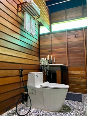 Un baño con una bañera independiente, paneles de madera, un lavabo pequeño y una planta colgante.