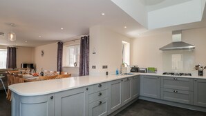 A modern kitchen with grey cabinetry, a central island, and a dining area with a table set for four. - Homeland (Somerton)