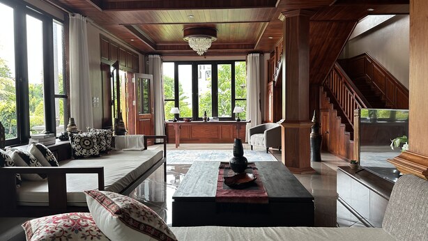 Un amplio salón con un gran ventanal, un conjunto de sofás, una mesa de centro y una escalera que sube a un nivel superior.